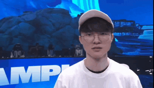 a man wearing glasses and a baseball cap is standing in front of a blue wall with the word amp written on it .
