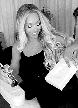 a black and white photo of a woman sitting on a couch holding a box and a book .