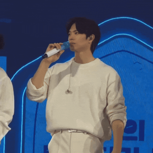 a man in a white sweater is singing into a microphone with a blue light behind him