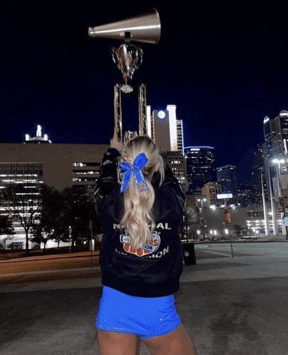 a cheerleader holds a trophy and a megaphone in front of a city skyline
