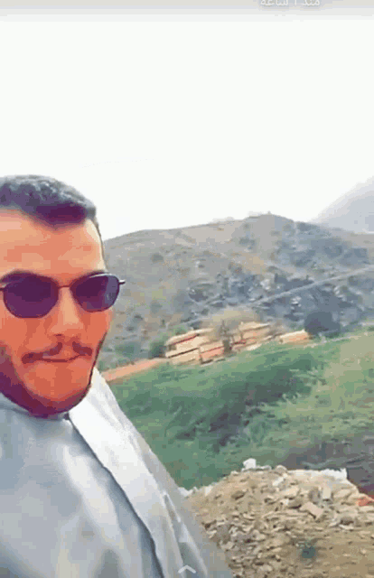 a man wearing sunglasses is taking a picture of himself in front of a mountain