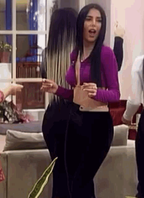 a woman in a purple shirt and black pants is standing in a living room with other women .