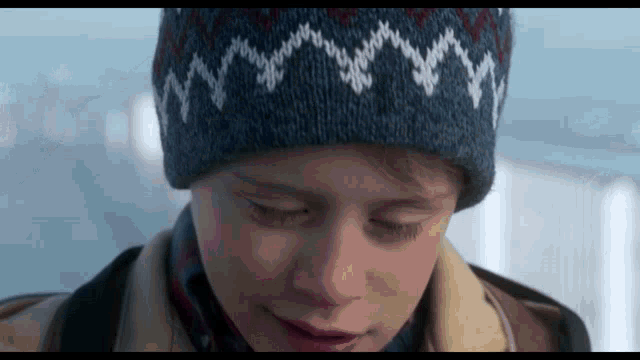 a close up of a boy wearing a knitted hat with mountains on it