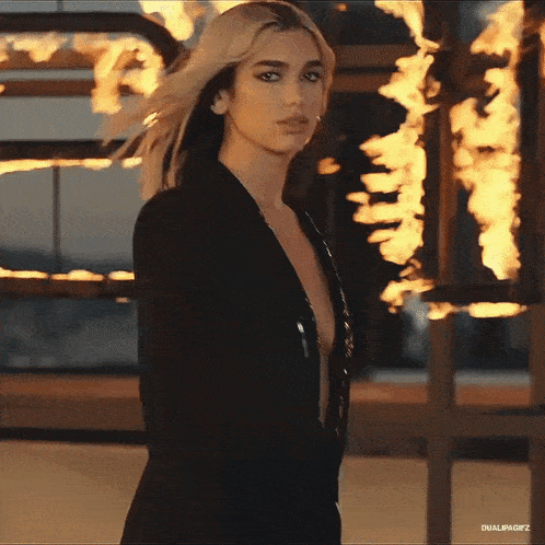 a woman in a black jacket is standing in front of a fire