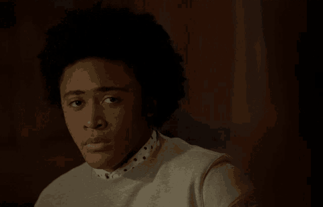 a young man with an afro wearing a sweater and polka dot shirt