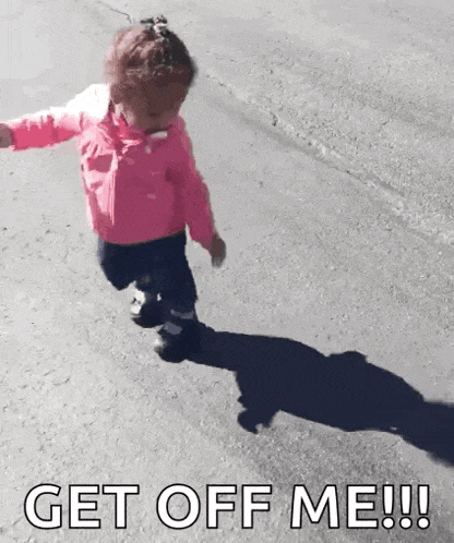 a little girl in a pink jacket is running down a street with the words get off me written on the ground .