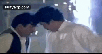 two men are standing next to each other and talking to each other in a dark room .