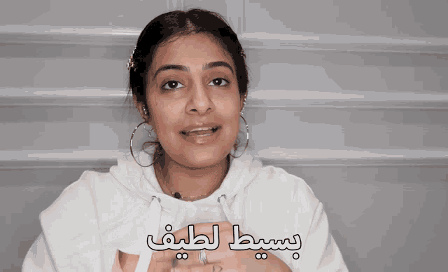 a woman wearing hoop earrings and a white hoodie with arabic writing