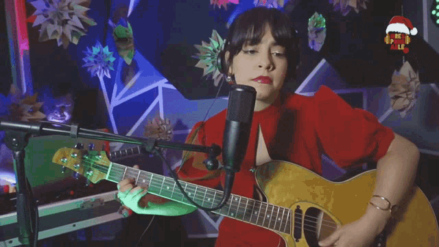 a woman singing into a microphone while playing a guitar with a santa hat hanging from the ceiling