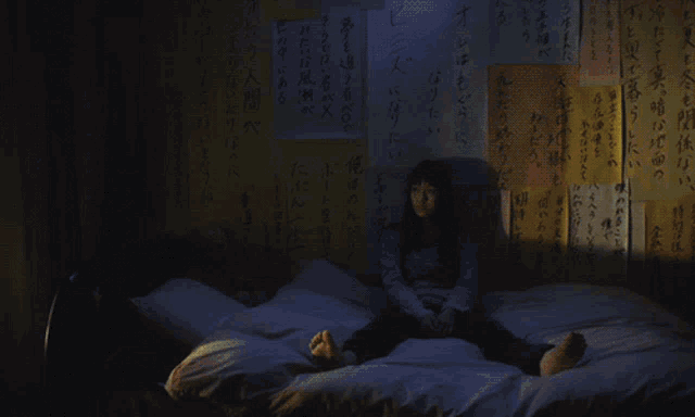 a girl sits on a bed in front of a wall with asian writing on it
