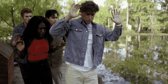 a group of people standing in front of a body of water with their hands in the air