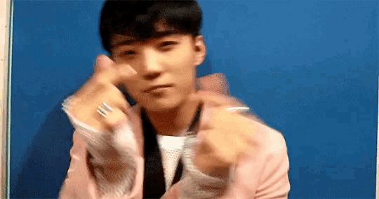 a man in a pink jacket is making a heart with his hands .