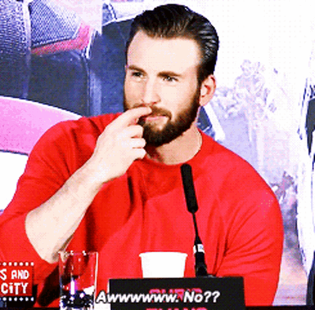 a man in a red shirt is sitting at a table with a sign that says awwwwww.no??