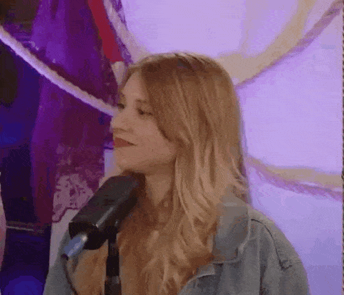 a woman in a denim jacket is standing in front of a microphone and smiling .