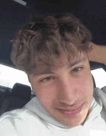 a young man with curly hair is sitting in the back seat of a car and smiling .