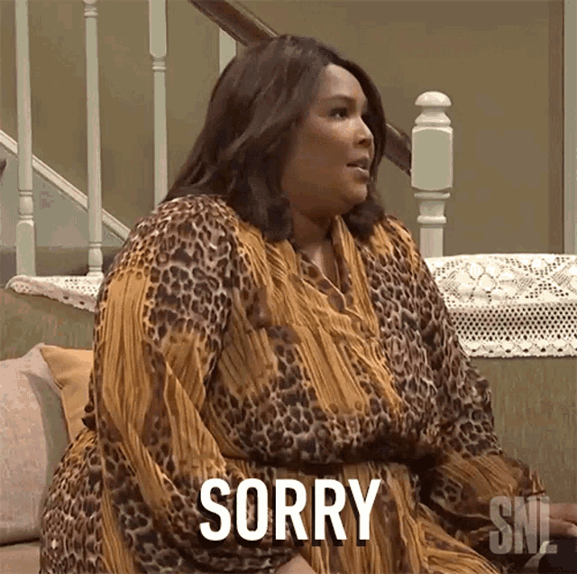a woman in a leopard print dress is sitting on a couch and saying sorry
