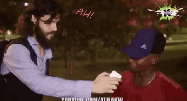 a man with a beard is giving a card to another man who is wearing a blue adidas cap