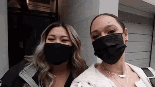 two women wearing face masks are standing next to each other and smiling .