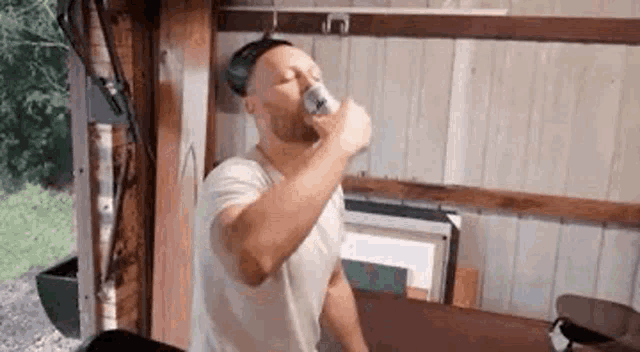 a man is drinking from a can of beer in a shed .