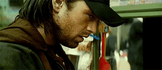 a man with long hair and a beard wearing a baseball cap is standing in front of a store .
