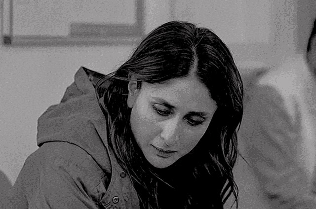 a black and white photo of a woman wearing a hooded jacket looking down .