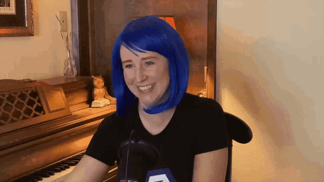 a woman wearing a blue wig is smiling while sitting at a piano