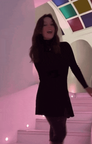 a woman in a black dress is dancing in a room with a colorful ceiling