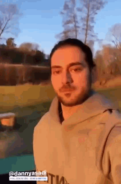 a man with a beard is taking a selfie in a park with trees in the background .