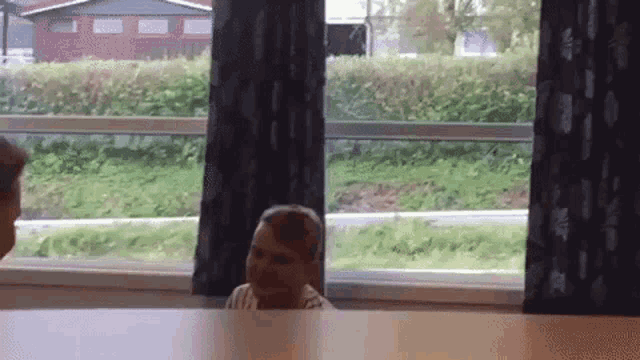 a boy is sitting at a table in front of a window