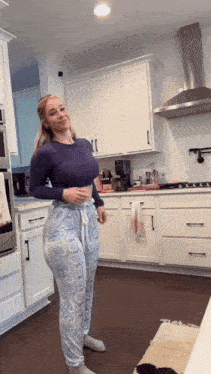 a woman is standing in a kitchen wearing pajamas and a purple shirt