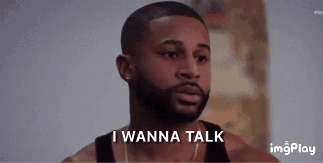 a man with a beard says " i wanna talk " while wearing a black tank top
