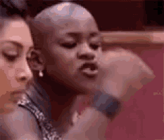a woman with a shaved head is sitting next to another woman and making a funny face .