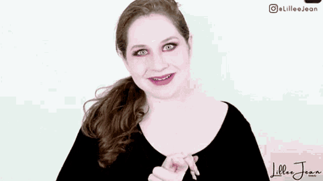 a woman is smiling and pointing at the camera while wearing a black shirt with the word tha on it .