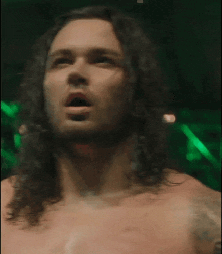 a shirtless man with long curly hair and a tattoo on his chest