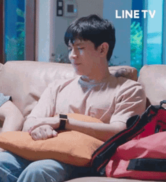 a man is sitting on a couch with a pillow in his lap and a line tv logo in the background