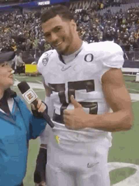 a man in a football uniform is giving a thumbs up while being interviewed by a woman .