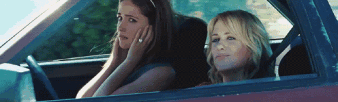 two women are sitting in a car one is talking on a cell phone