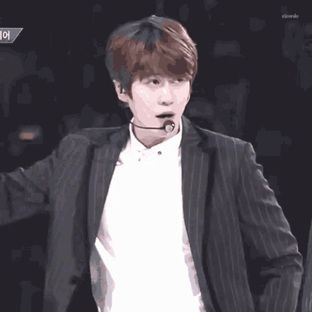 a young man in a suit and white shirt is standing on a stage with a microphone in his mouth .