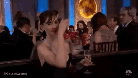 a woman in a black dress is sitting at a table with a glass of wine in her hand .