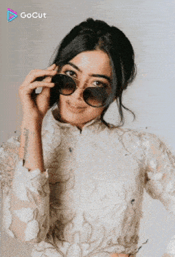 a woman wearing sunglasses and a white top has a tattoo on her wrist that says ' gocut '