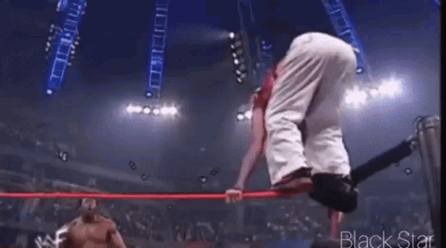 a wrestling match is being held in a stadium and a wrestler is jumping over the ropes .