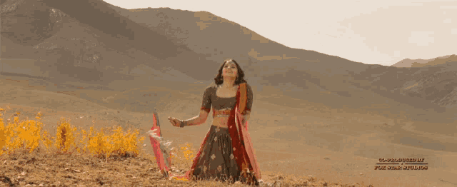 a woman in a crop top and skirt is kneeling in the dirt in front of mountains