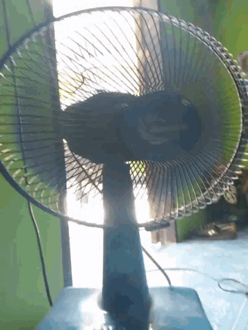 a fan is sitting on a table in front of a window with the sun shining through it
