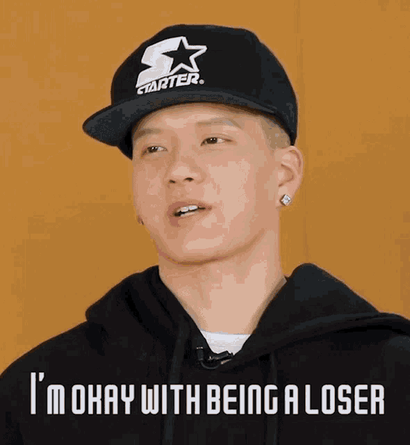 a man wearing a starter hat and a black hoodie says i 'm okay with being a loser