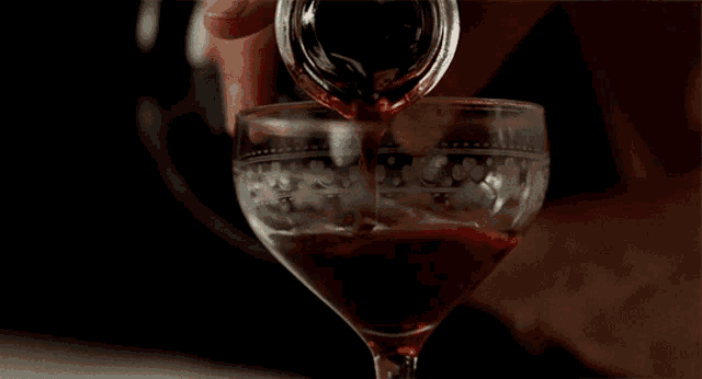 a person pouring a drink into a glass with a floral design