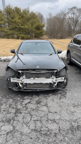 a black car with a damaged front bumper is parked in a parking lot