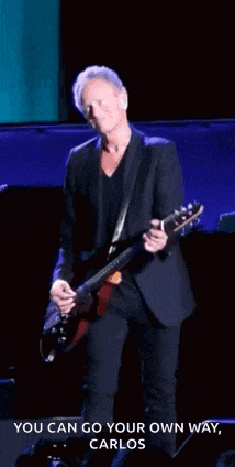 a man in a suit is playing a guitar on a stage with a caption that says you can go your own way carlos