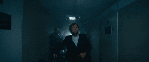 a man in a suit is standing in a dark hallway with his hand up .