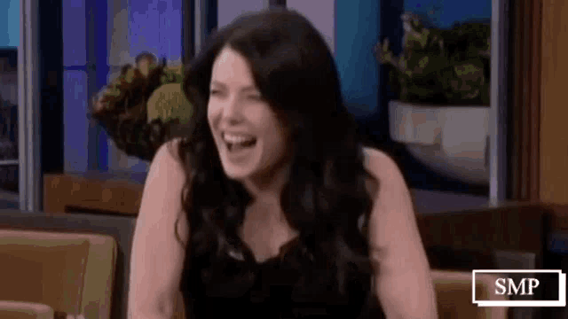 a woman in a black dress is laughing while sitting on a chair .