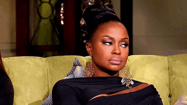 a woman in a black dress is sitting on a green couch looking at the camera